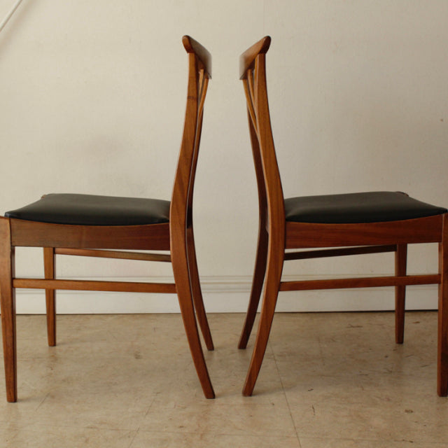 Pair of vintage G-Plan teak dining chairs with curved mid-century British design and black padded seats.
