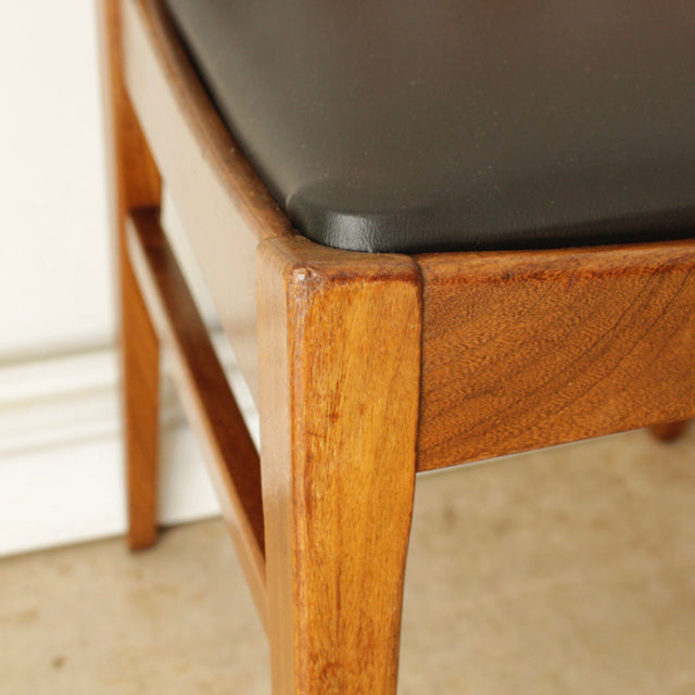 Close-up of vintage British mid-century G-Plan dining chair with teak wood frame and black leather seat cushion, showcasing.