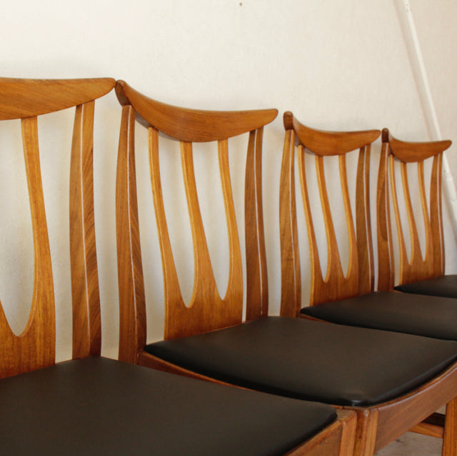 Set of four vintage G-Plan teak dining chairs with British mid-century Denmark-inspired curved backs and black cushioned.