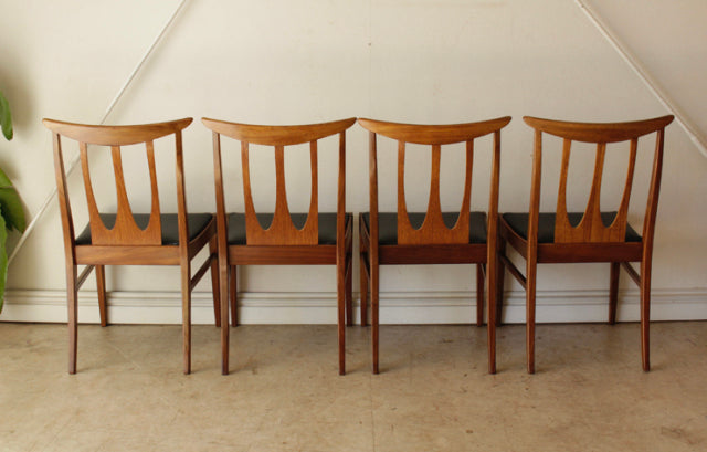 Set of four vintage G-Plan teak dining chairs with British mid-century design, slender legs, and distinct open backrests.