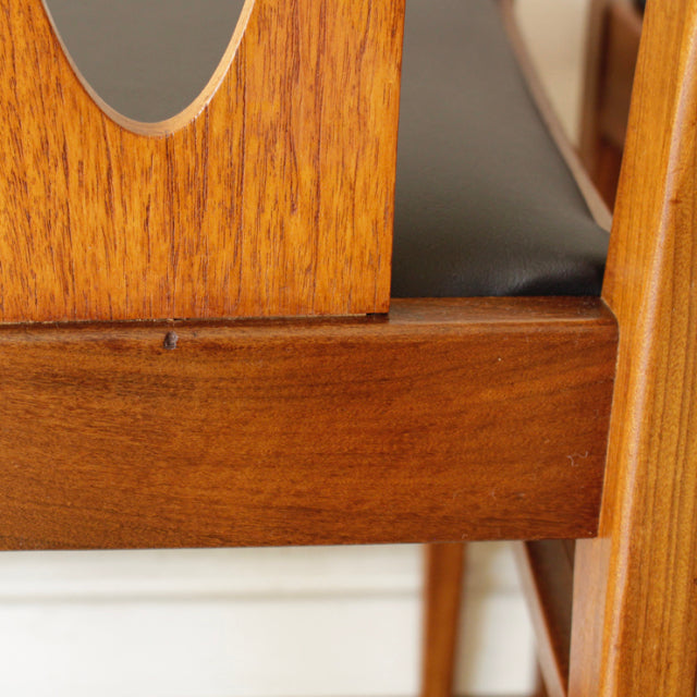 Close-up of vintage British G-Plan teak dining chair showing rich wood grain, smooth mid-century frame, and dark upholstered .