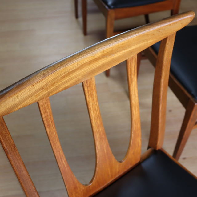 Set of four vintage G-Plan mid-century teak dining chairs with curved backrests and black cushioned seats, showcasing.