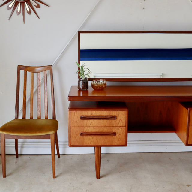Vintage British G-Plan teak mid-century desk with rich wood grain, tapered legs, and compact drawers, paired with a mustard.