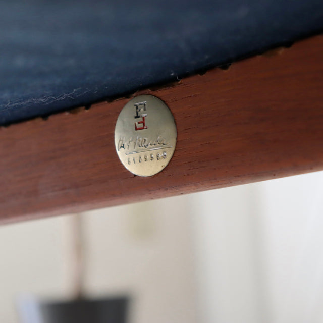 Close-up of brass Peter Hvidt & Orla Molgaard-Nielsen model148 badge on vintage teak frame with dark upholstery, mid-century .