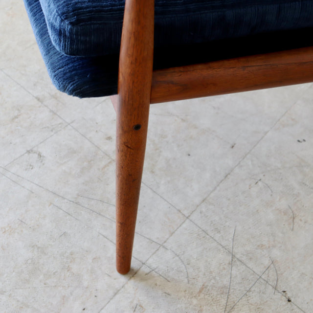 Mid-century teak sofa leg with visible wood grain supporting deep blue upholstered seat, vintage Danish design.