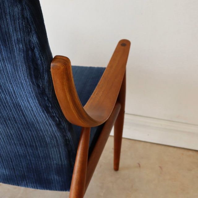 Mid-century Danish teak armchair with smooth curved armrest and rich blue velvet upholstery, showcasing fine wood grain and.