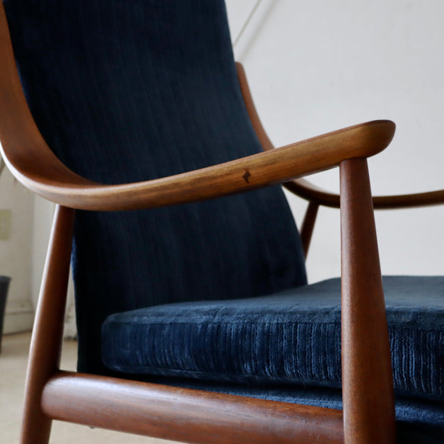 Vintage mid-century Danish teak chair with curved armrests and navy blue high-back upholstery, showcasing smooth wood grain.