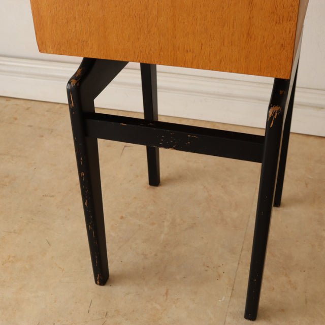 Close-up of vintage British mid-century teak bedside cabinet leg with black-painted slender wood showing worn paint and rich .