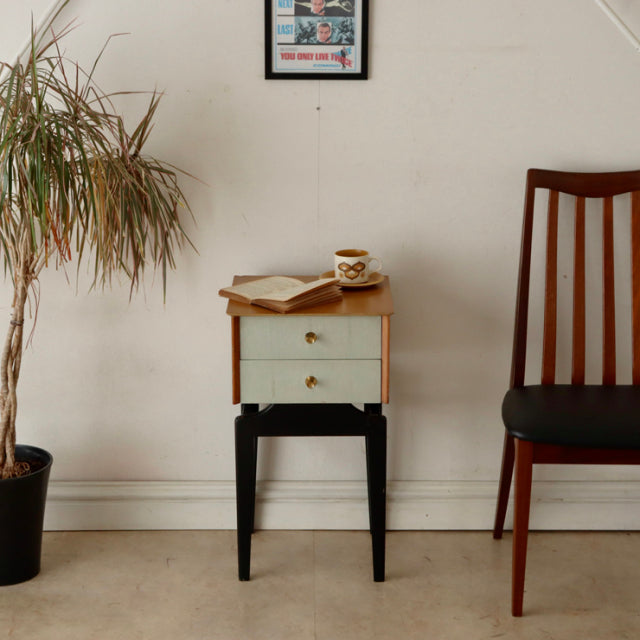 Vintage British mid-century teak bedside cabinet with sleek wood grain, light blue drawer fronts, brass knobs, and slender.