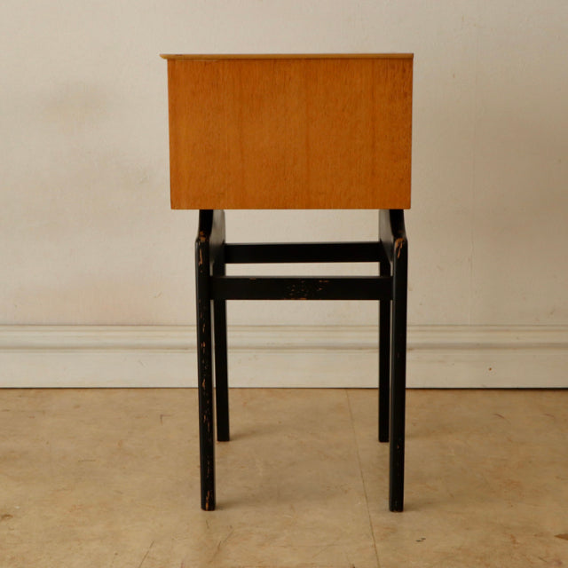 Vintage British mid-century teak bedside cabinet with visible wood grain, slim black legs, and clean rectangular form.