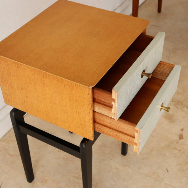 Mid-century British vintage teak bedside cabinet with black legs and two white drawer fronts featuring brass knobs,.