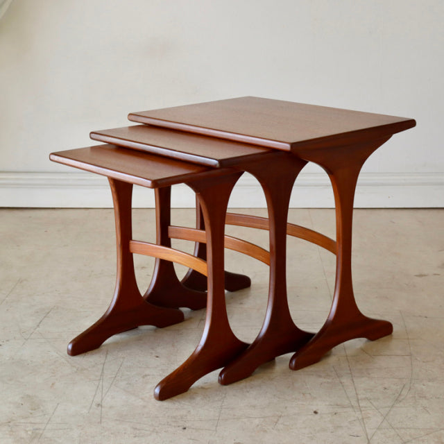 Set of three vintage British G-Plan teak nest tables with smooth wood grain and sculpted mid-century Denmark-style legs.