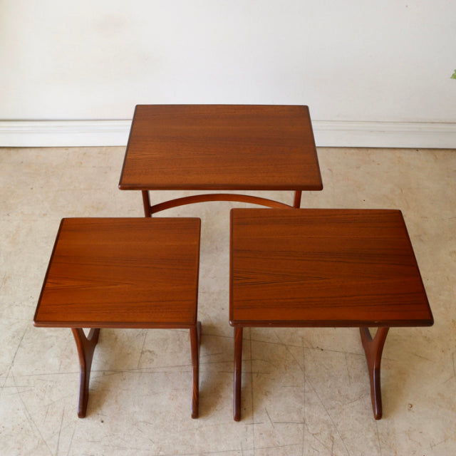 Set of three vintage G-Plan teak nest tables with smooth wood grain, tapered legs, and mid-century British design.