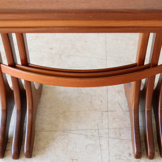 Set of three vintage teak G-Plan British mid-century nest tables with curved edges and tapered legs showing rich wood grain.