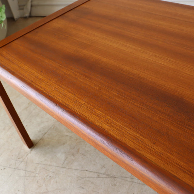 Vintage teak coffee table with smooth wood grain, British mid-century style, slender angled legs, clean rectangular form,.