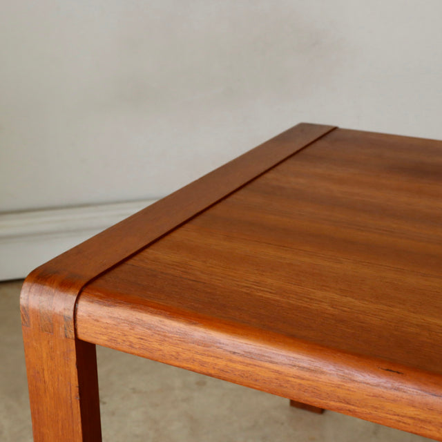 Vintage British mid-century teak coffee table corner with smooth rounded edges and visible wood grain.
