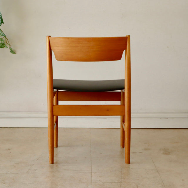 Mid-century British vintage teak dining chair from Denmark with smooth wood grain and black upholstered seat viewed from back.