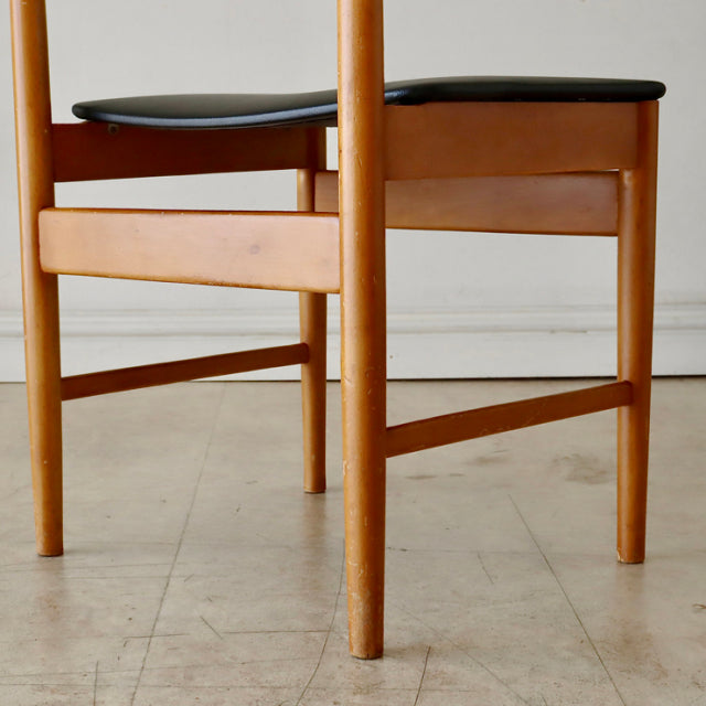 Mid-century British vintage teak dining chair with smooth wood grain and black padded seat, elegant tapered legs.