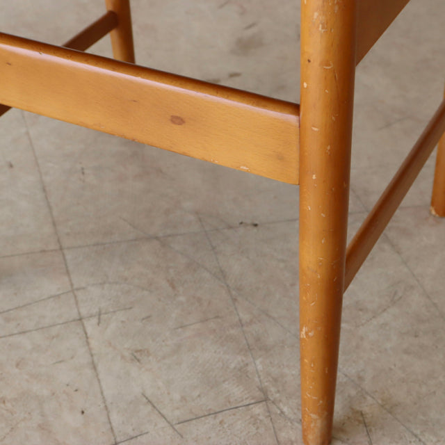 Close-up of vintage teak dining chair leg with mid-century British design, smooth wood grain, and tapered form.
