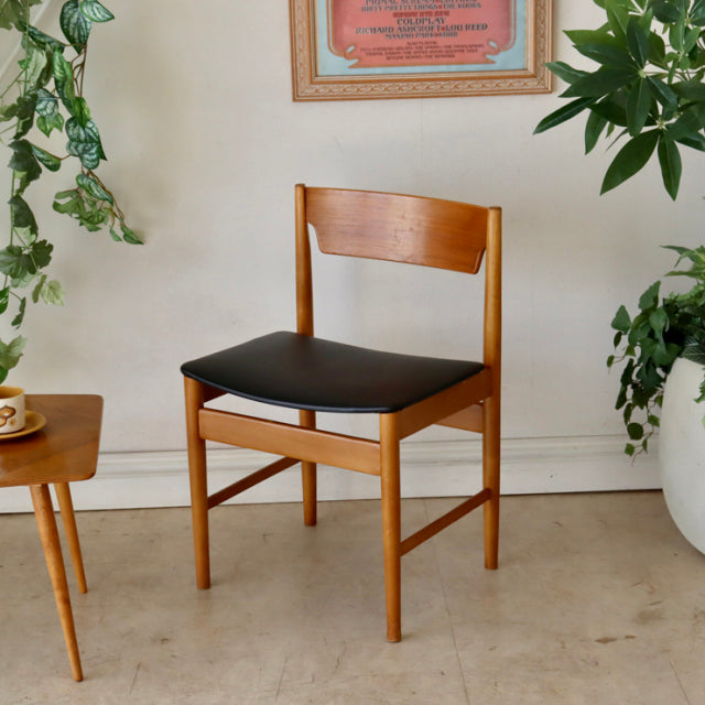 Mid-century British vintage teak dining chair with sleek wood grain and black upholstered seat, Danish design influence.