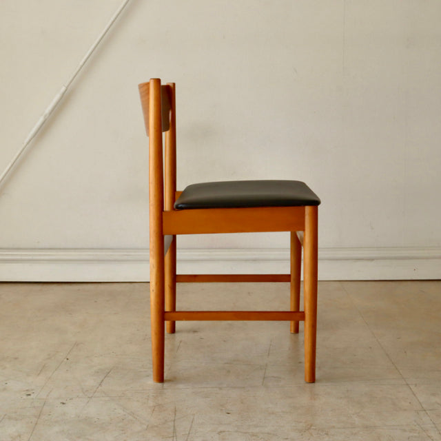 Mid-century British vintage teak dining chair with black cushioned seat and sleek wooden frame.