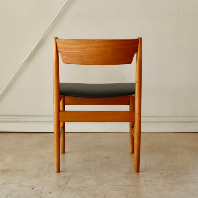 Mid-century British vintage teak dining chair with smooth wood grain and black upholstered seat viewed from back.