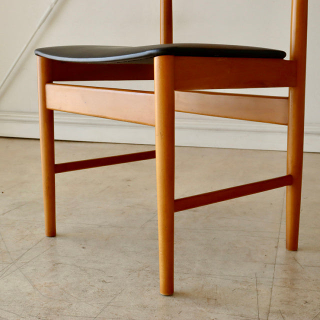 Vintage mid-century British teak dining chair with smooth wood grain and black upholstered seat, slender round legs and.