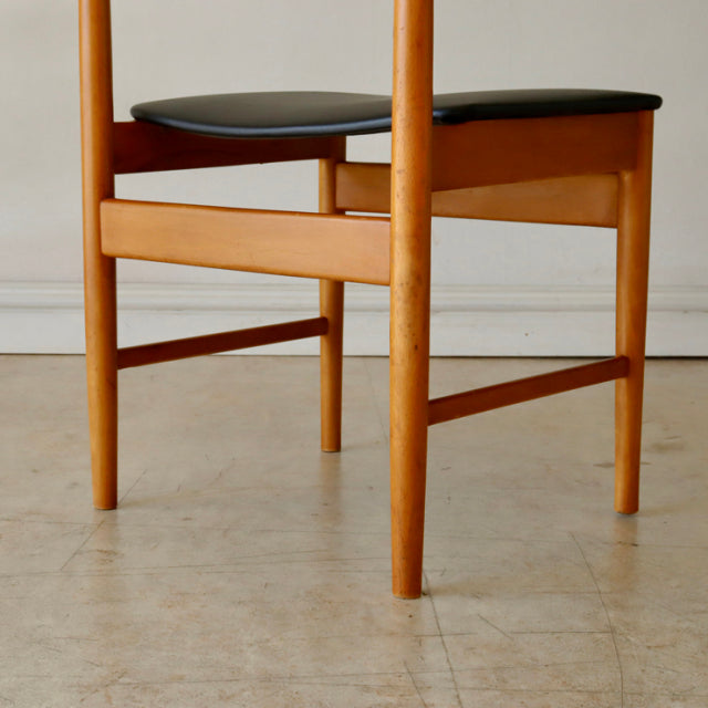 Vintage mid-century British teak dining chair with smooth wood grain, rounded legs, and black upholstered seat from Denmark.