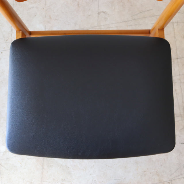 Vintage British mid-century teak dining chair with smooth black reupholstered seat and sleek wooden frame.