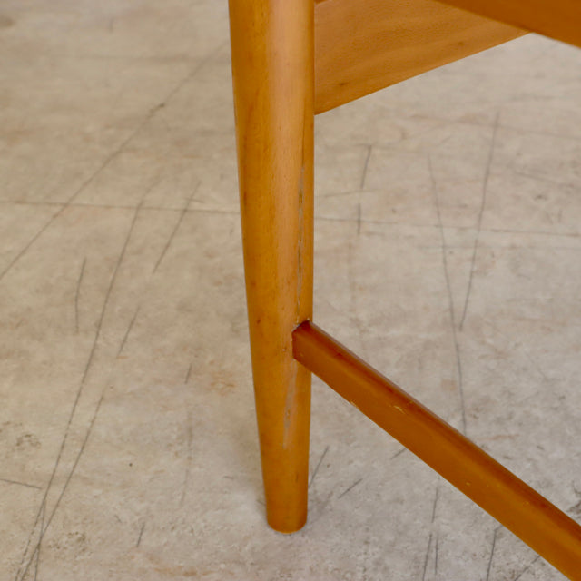 Mid-century British vintage teak dining chair leg with smooth wood grain and clean finish on a worn concrete floor.