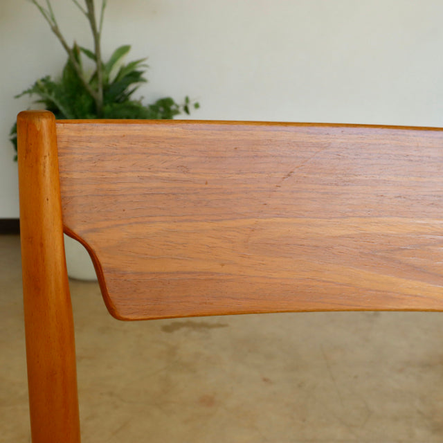 Close-up of vintage mid-century teak dining chair backrest with smooth wood grain and rounded edges, British and Danish.