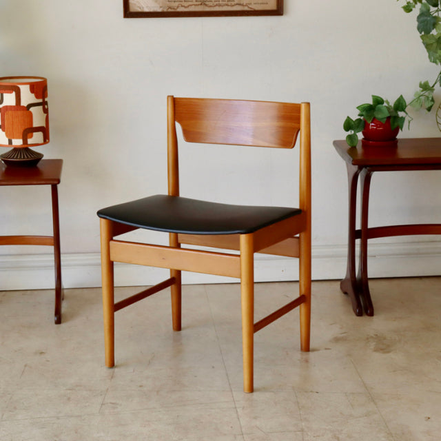 Mid-century British vintage teak dining chair with black upholstered seat and clean wood grain.