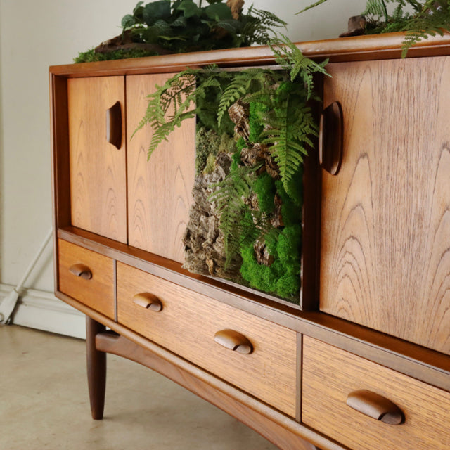 Mid-century British G-PLAN teak sideboard with rich wood grain, sculpted handles, and tapered legs, featuring a vibrant.