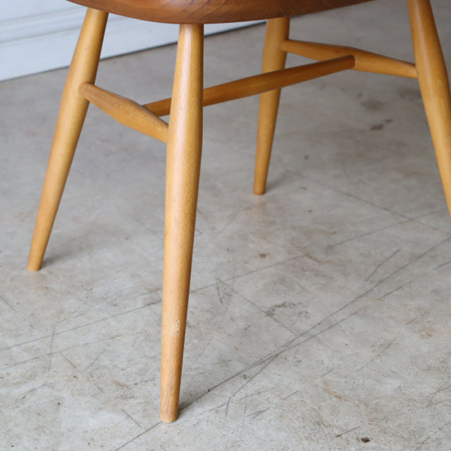 Close-up of natural teak wood leg and stretcher of mid-century British Ercol Quaker chair showing smooth grain and rounded.