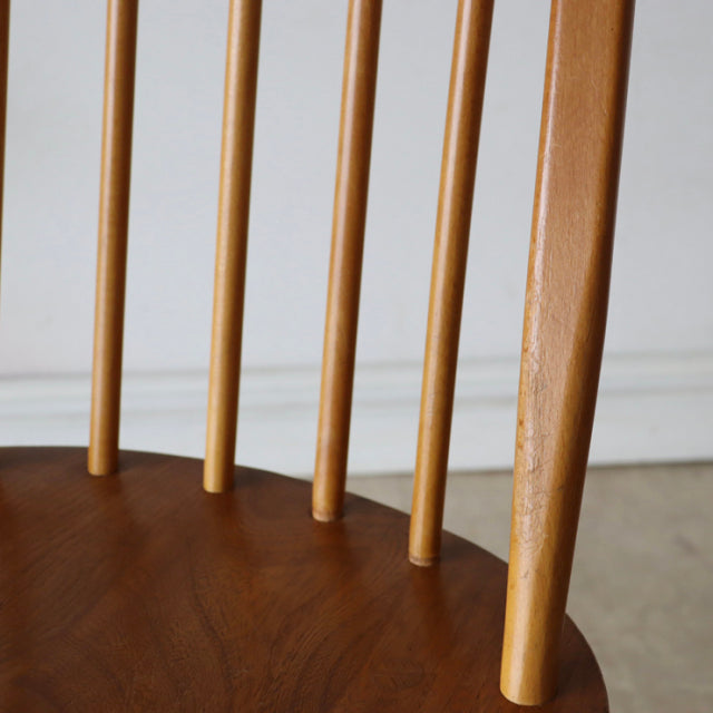 Close-up of mid-century British Ercol Quaker chair in natural teak with smooth wood grain and slender vertical spindled.