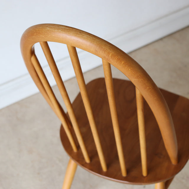 Vintage Ercoll mid-century British teak dining chair with curved spindle backrest and smooth natural wood grain.