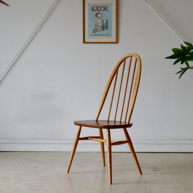 Vintage British Ercol Quaker chair in natural teak with curved spindle back, tapered legs, and smooth wood grain,.