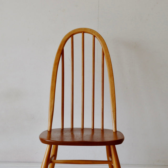 Vintage British mid-century Ercol Quaker chair in natural teak with curved spindle back and visible wood grain.