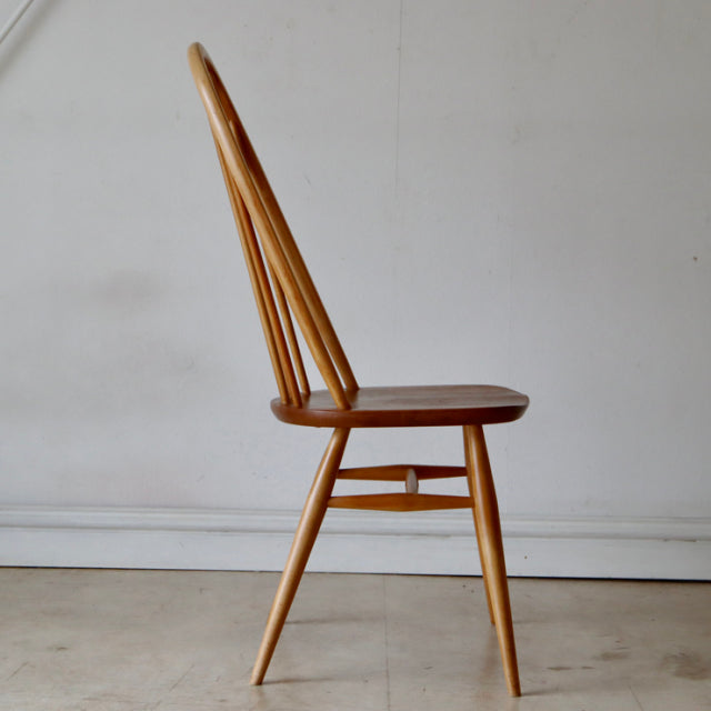 Mid-century British ERCOL Quaker chair in natural teak with slender spindled back and angled legs showcasing visible wood.