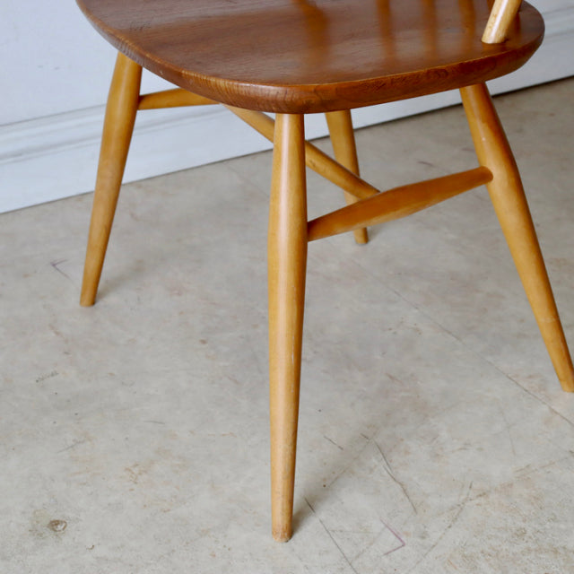 Mid-century British vintage Ercol Quaker chair in natural teak with smooth rounded seat and tapered legs showing fine wood.