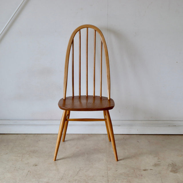 Vintage mid-century British Ercol Quaker chair in natural teak with curved spindle back and rounded seat.
