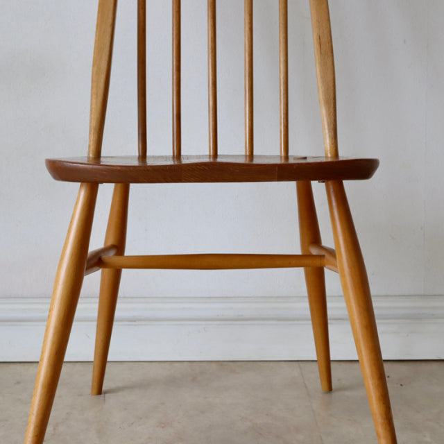Mid-century British Ercol Quaker chair in natural teak with smooth curved seat, slender spindle back, and tapered legs.