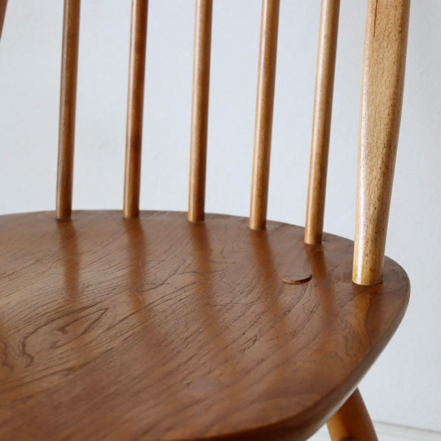 Close-up of vintage ERCOL Quaker chair in natural teak with smooth curved seat and slender tapered spindled backrest in.