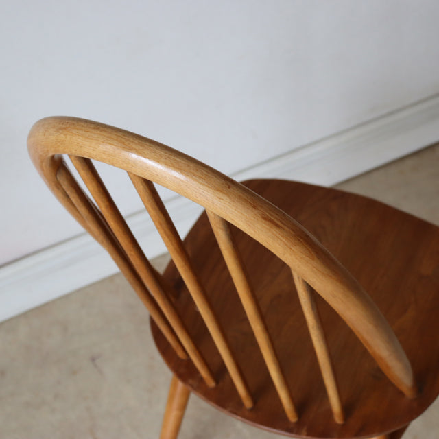Vintage British mid-century Ercol Quaker chair in natural teak with curved spindle back and visible wood grain.