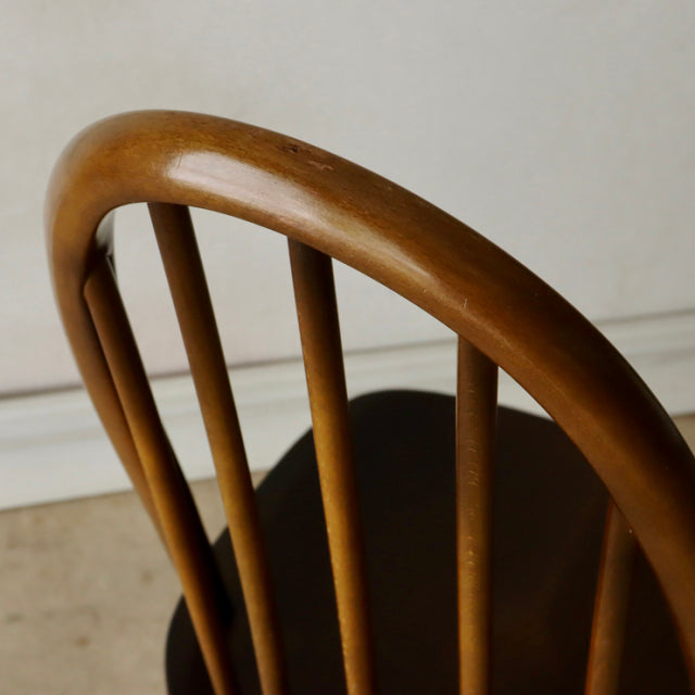 Vintage mid-century British Ercol Quaker dining chair in warm teak with curved spindle backrest and visible wood grain.