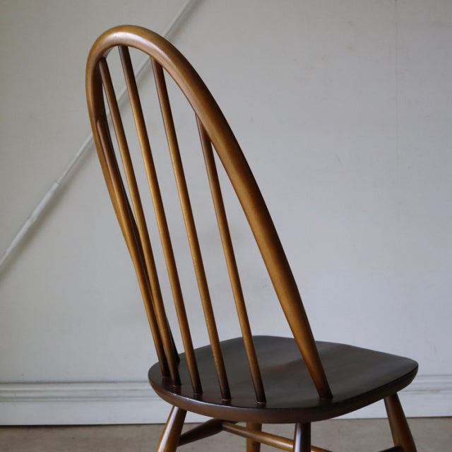 Vintage British Ercol Quaker chair in warm teak with mid-century curved back spindles and smooth wood grain seat.