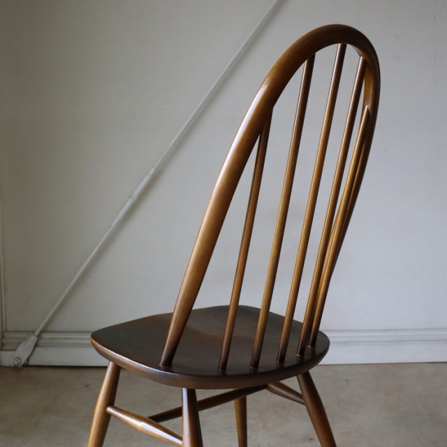 British mid-century ERCOL Quaker chair in warm brown teak with a curved spindle back and smooth rounded legs.