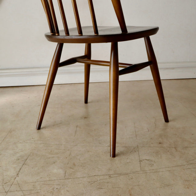 Mid-century British Ercol Quaker chair in teak with slender spindle back and tapered legs showing warm wood grain.