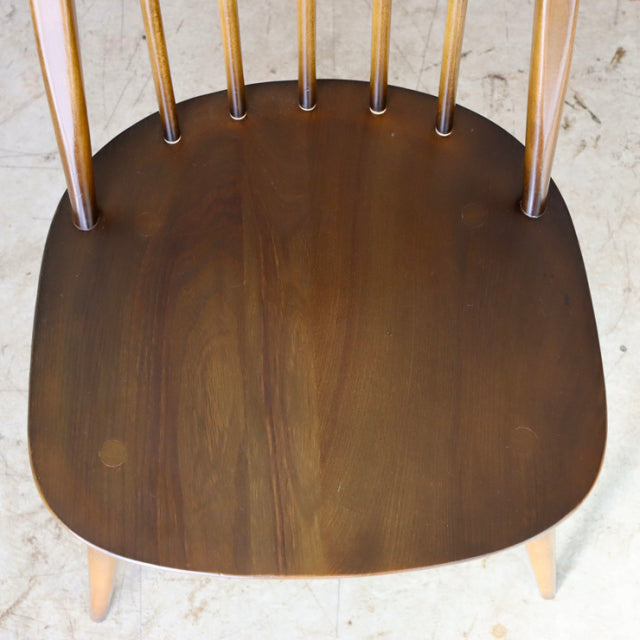 Mid-century British Ercol Quaker chair with smooth teak seat, spindled backrest, and light wooden legs.