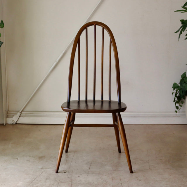 British mid-century ERCOL Quaker chair in teak with curved spindle backrest and tapered legs showing smooth wood grain in.